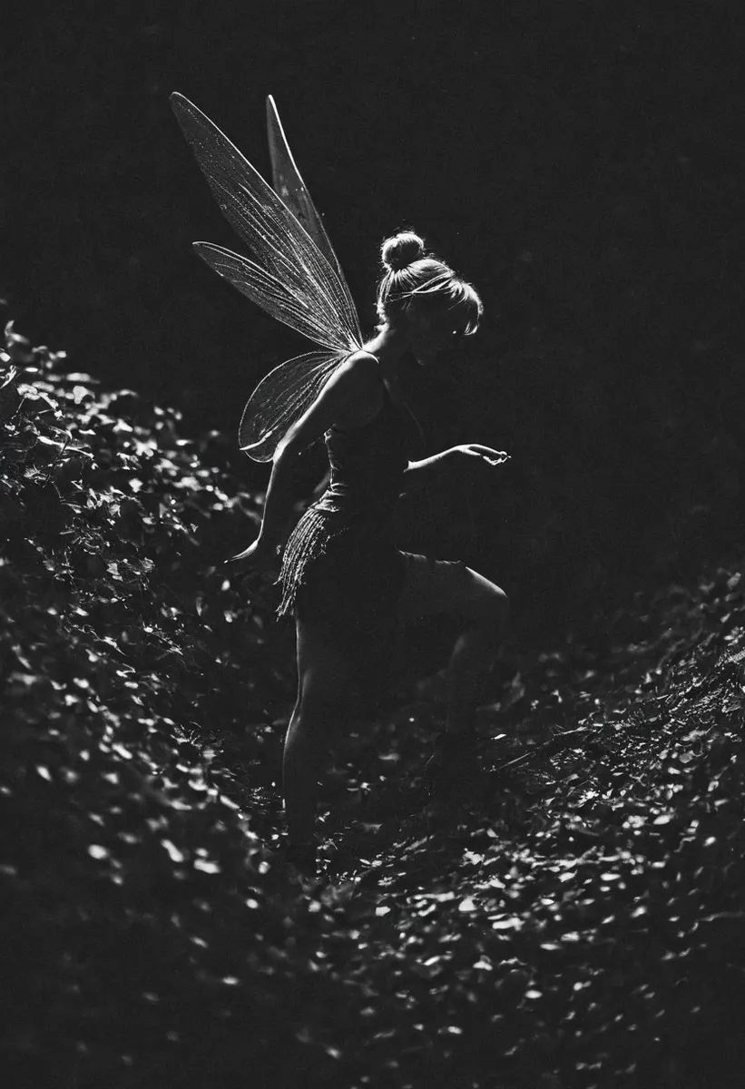 Black and white high-contrast silhouette of a woman with delicate fairy wings, resembling Tinkerbell, stepping through a leafy area with cinematic lighting and subtle grain.