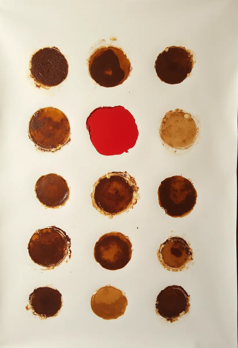 Minimalistic collage of multiple coffee cup circle stains on white paper with one bold red circle in the center