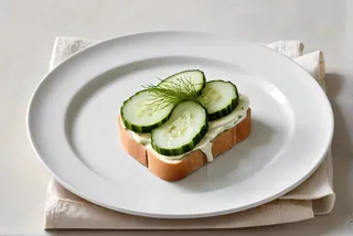 Top view of a cucumber sandwich with white bread and mayo on a white plate, featuring a minimalistic and clean background.