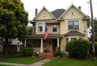 Yellow American style house with an American flag on the porch, surrounded by a green front lawn and trees