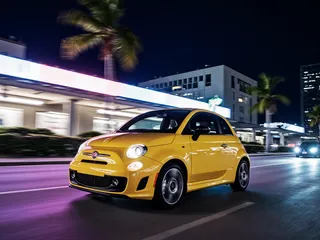 Yellow Fiat 500 car driving fast on a Miami street at night with motion blur, neon lights, and palm trees in the background.
