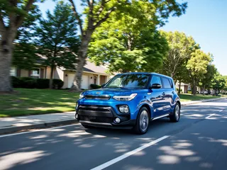 Blue Kia Soul driving fast with motion blur on a sunny day in a suburban neighborhood with oak trees and blue sky