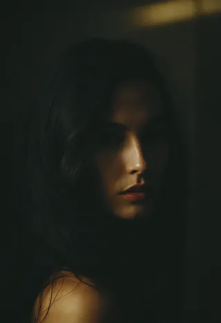Low key sensual portrait of a mysterious woman with soft and fuzzy lighting highlighting her face and shoulder, creating an emotional and intimate mood.