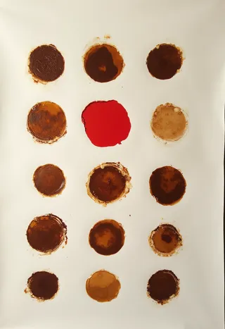 Minimalistic collage of coffee cup circle stains in various shades of brown with one bold red circle, arranged in a pattern on white paper.