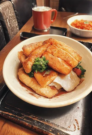 Close-up of a cozy restaurant food dish featuring fried tofu, garnished with leafy greens, served in a white bowl on a rustic tray, with a warm-toned mug and another bowl in the background.