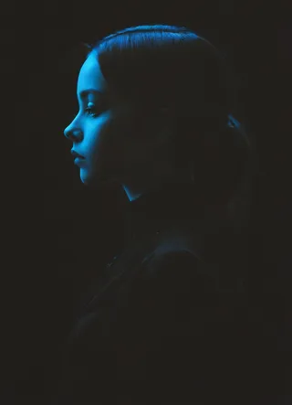 Profile silhouette portrait of a woman illuminated with blue low-key lighting against a dark background.