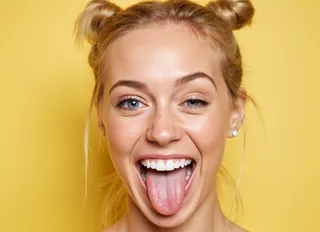 Close-up of a playful young woman with medium-toned skin and light blue eyes, blonde hair styled in two bunches, sticking out her tongue against a yellow background.