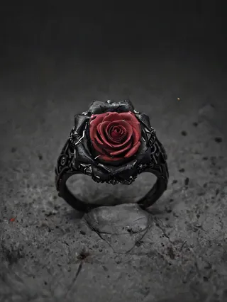 A black ring holding a red rose as its centerpiece, set against a dark, textured background with deep shadows.